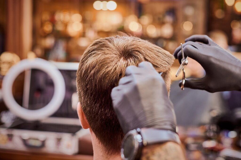 Male haircut in barbershop close up, client getting haircut by hairdresser with comb and scissors